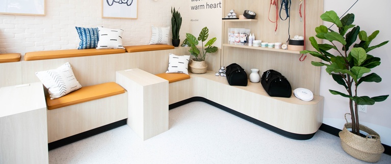 A clean and modern veterinary clinic waiting area with a bench, pet-themed decorations, and a "wet nose, warm heart" slogan on the wall.