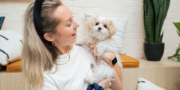 A woman holding a small dog indoors while looking at it affectionately.